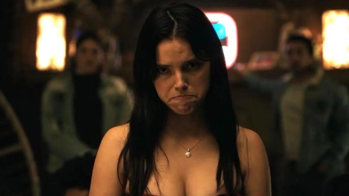 A young woman with long dark hair stands in a dimly lit bar, making a pouting, disappointed face. Her dejected expression humorously captures the frustration of a crypto investor watching the stock market reach new highs while their portfolio remains stuck elsewhere.
