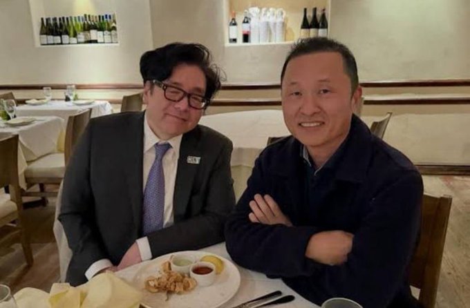 Two men pose for a photo in what appears to be a restaurant, with one wearing a suit and tie while the other wears a dark sweater, sitting at a table with food and condiments. The accompanying post references Chairman Kim Seungho and selling timing for Bitmine (BMNR) stock, suggesting the image likely depicts him at a meeting or meal related to this discussion.