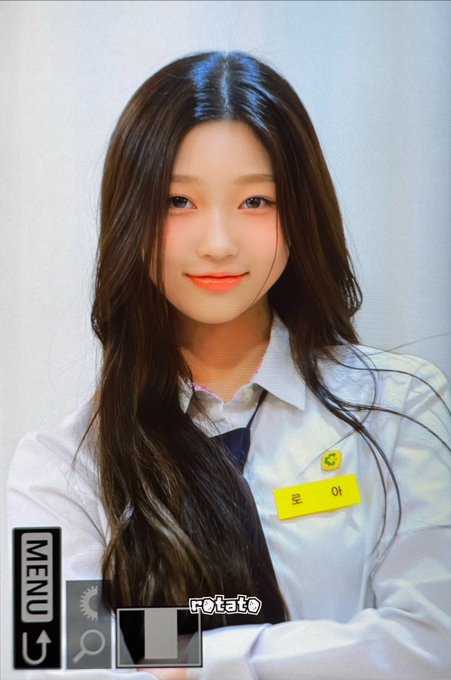 A photo of a young woman with long dark hair wearing a white shirt and a yellow name tag reading 'ho', with 'MENU' and 'rotate' interface elements overlaid on the image.