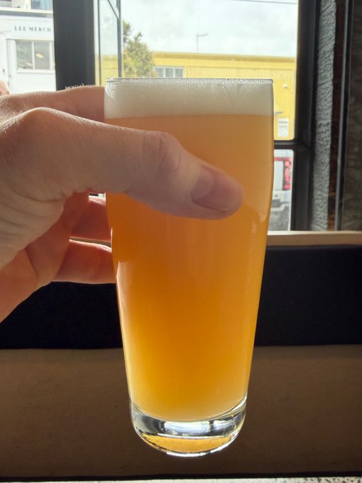 A hand raises a glass of hazy beer in a toast, with "LEE MERCH" visible on a building through the window behind, as a Friday cheers to the "intolerant, toxic Bitcoin monetary maximalist Knots node runners" rallying hash rate behind BIP-110.