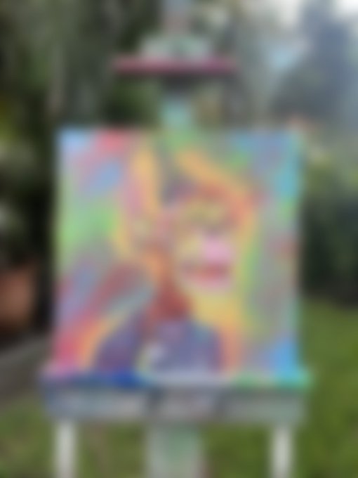 A blurry, out-of-focus image of a colorful painting on an easel set up outdoors in a grassy area.