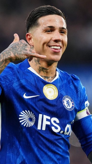 Enzo Maresca, the Chelsea midfielder wearing the blue kit with "IFS" sponsor and the FIFA Club World Cup champion badge, flashes a smile and gestures toward his ear — likely soaking in the crowd, unaware that transfer rumors link him to a £120M move to Manchester City.