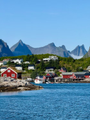 A small, low-resolution photo depicts a coastal village with colorful houses on rocky terrain, set against a backdrop of sharp mountain peaks and a blue body of water.