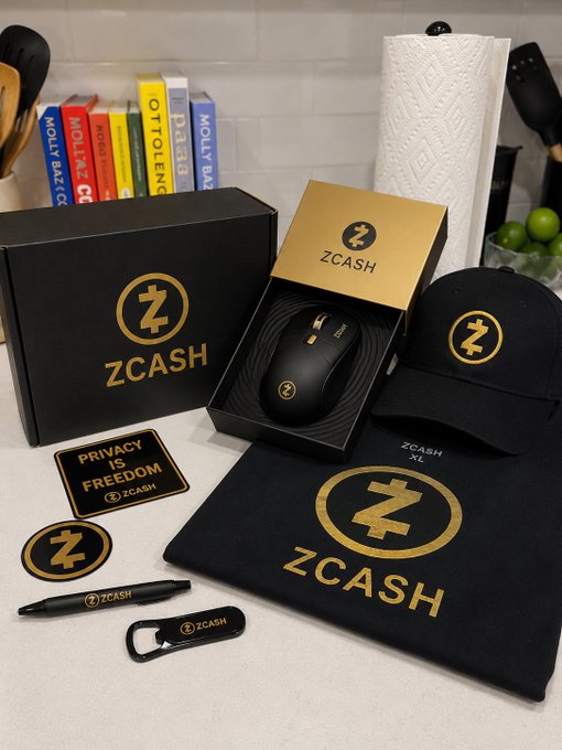 The image features a collection of items, including a mouse, keyboard, hat, t-shirt, and other accessories, all branded with the Zcash logo. The items are displayed on a table or countertop, suggesting that they might be part of a promotional event or merchandise sale. The post includes text that reads "yoooo thank you @Zcash for the swag me and my brother are gonna wear it out to the gay club tonight". This implies that the Zcash brand is being used as a gift item or promotional item, possibly for an upcoming event like a gay pride celebration.