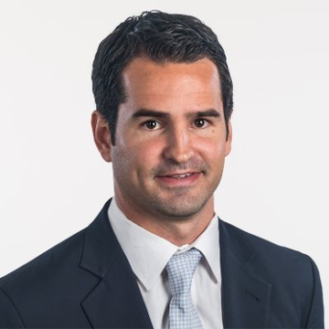 The image features a man dressed in a suit, tie, and white shirt with black hair. He has a serious expression as he looks directly at the camera. The background of the photo is plain white, which makes him stand out even more. There are no other objects or people visible in the image, and it does not contain any text.