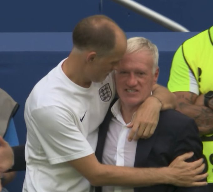A young soccer player in a white England jersey embraces a man in a dark suit, who grimaces intensely.