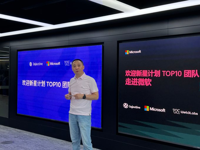 A man stands in front of screens displaying "欢迎新星计划 TOP10 团队 走进微软" alongside logos for Injective, Microsoft, and web3Labs, welcoming the top 10 teams into Microsoft's offices as part of the Injective Nova Program—an initiative that supports and educates developers and founders in the Web3 space.