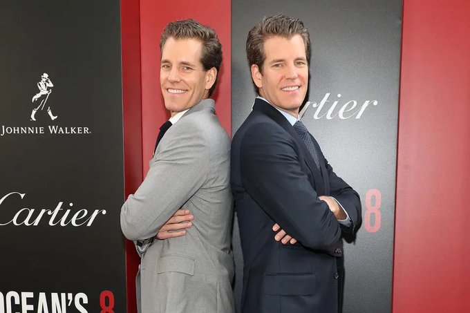 Actors wearing suits pose back-to-back in front of a red backdrop, with Johnnie Walker and Cartier logos visible, suggesting an 'Ocean's 8' promotional event.