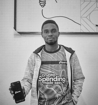 A man poses in front of a wall art piece at a MetaMask Community Builders Night, wearing a t-shirt with the "crypto Spending made easy Spenda" logo and holding up a Spenda-branded card. His MetaMask-hosted event attire and the branded card tie directly into the post about connecting with fellow Web3 builders in the community.