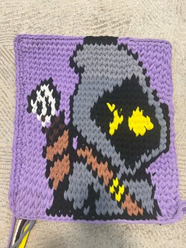 A crocheted square featuring a pixelated Star Wars Jawa character in a gray hooded robe with glowing yellow eyes, set against a purple background.
