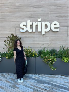 A woman in a black outfit poses in front of a 'stripe' company sign at what appears to be their office building.