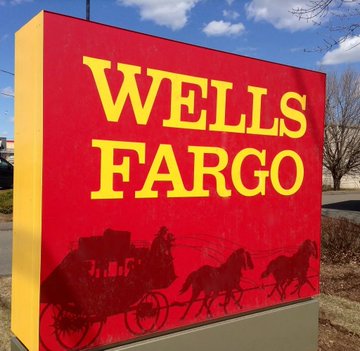 A vibrant red and yellow Wells Fargo bank sign features the company's name in bold lettering above a silhouette of a horse-drawn stagecoach. The image relates to the post by symbolizing traditional banking and financial services, which contrasts with the discussion of unconventional investment strategies and crypto-related assets like $MSTR mentioned in the caption.