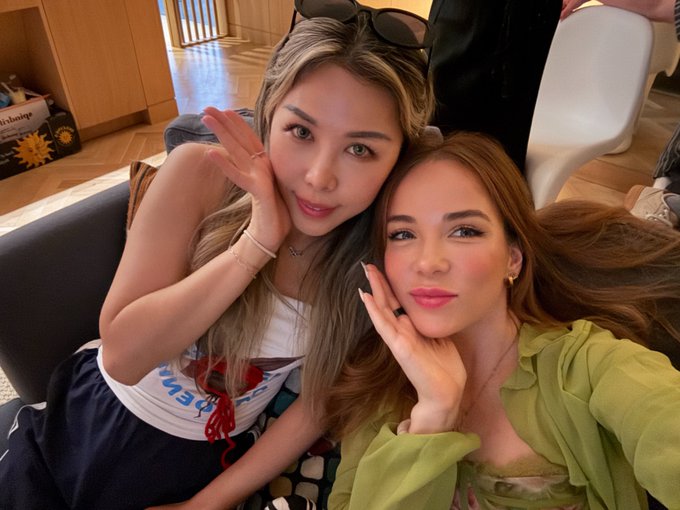 The image features two women sitting next to each other on a couch, both smiling for a photo. One of them has her hand on her face while posing for the picture. The background includes a chair and a dining table, suggesting that they are in someone's home or living space. The caption provided seems unrelated to the main focus of the image - the two women sitting together and enjoying each other's company.