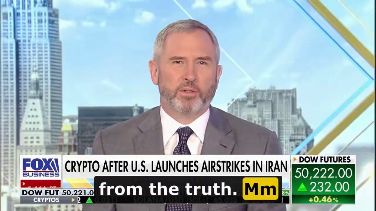 The image shows a man wearing a suit, sitting at a desk or podium while talking about cryptocurrency and its impact on the economy. The background features a city skyline with tall buildings, suggesting that this discussion might be taking place in an urban setting. The text "Crypto after U.S. launches air strikes in Iran" is prominently displayed, indicating that the man is discussing the use of cryptocurrency for funding military operations or other purposes related to warfare.