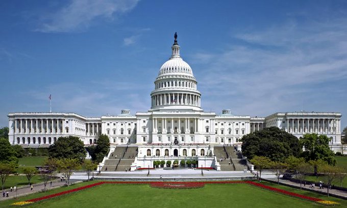 The image shows a large white building with multiple windows, possibly a government building or courthouse, situated next to a park. A person can be seen walking near the entrance of the building. In addition to this scene, there are red flowers scattered throughout the area, adding color and life to the setting. The content of the post suggests that the US Government has decided to invest in Alameda Research's assets by moving $800,000 from theirFTX estate to compensate users and creditors affected by a failed real estate project.