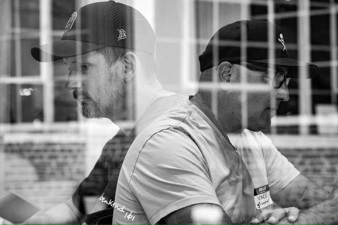 A black-and-white double exposure photograph showing the overlapping profiles of two men wearing baseball caps, one with 'thankful 101' on his shirt and the other wearing sunglasses with a 'VANS' logo.