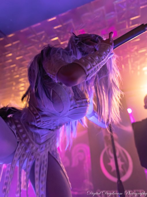 Concert photo of a performer in an ornate white studded outfit and long blonde hair, holding a microphone under purple stage lighting, watermarked 'Digital Daydream Photography'.