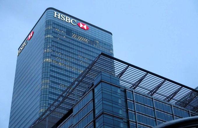 A tall modern glass skyscraper displays the "HSBC" logo with its red and white hexagon symbol at the top, viewed from below against a clear sky.
