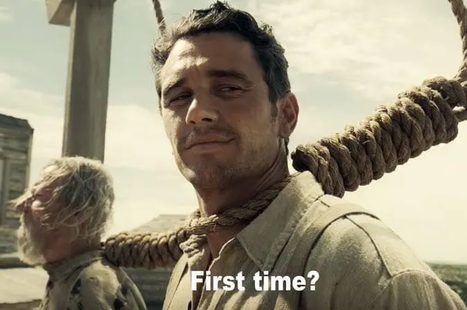 A scene from a film shows a man with a noose around his neck smiling slightly, with the text "First time?" overlaid.