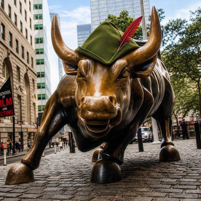 The iconic Wall Street Charging Bull statue is humorously adorned with a green Robinhood-style beret and red feather, symbolizing the Robinhoob Bull meme coin. The accompanying text "CA: 0xa98386f12b3fc8b08fb4a2c78fe361eba60dd5f6" provides the contract address for the meme token inspired by this rebellious stock-market imagery.