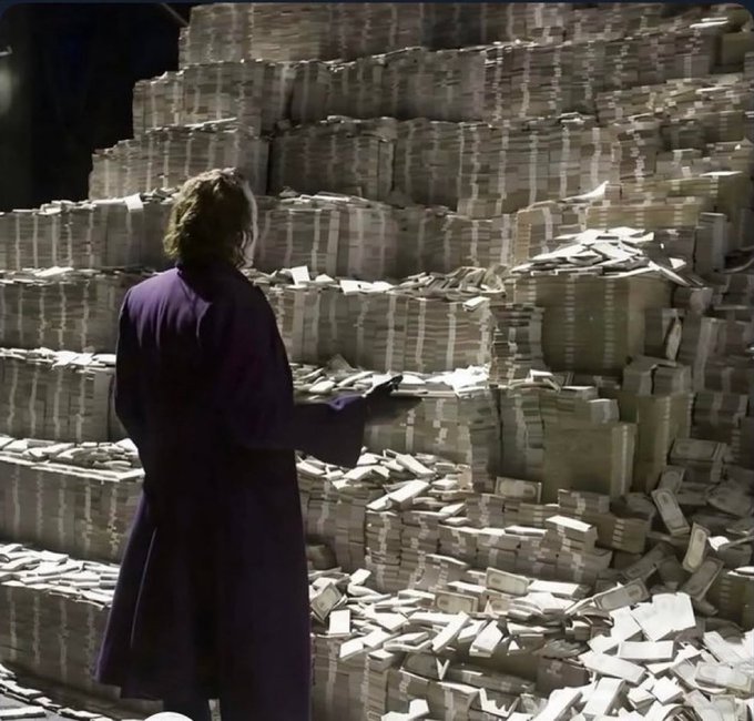 The Joker, with his back turned and wearing a purple coat, stands before massive piles of stacked and scattered money. The image perfectly captures the post's "POV: you bought the right memecoin" sentiment, visually representing the overwhelming wealth one would feel after making a successful crypto investment.