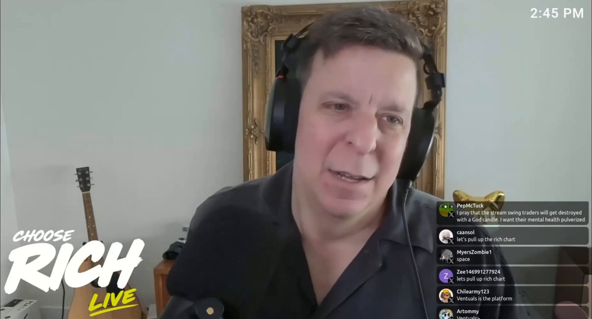 The image shows a man wearing headphones sitting at a desk or table while talking into a microphone. The background of the image features a white wall with a framed picture hanging above him, as well as an open laptop nearby. A caption on the screen reads "Choose Rich Live", which suggests that this is part of a streaming platform where people can watch and participate in discussions about various topics related to wealth and personal finance.