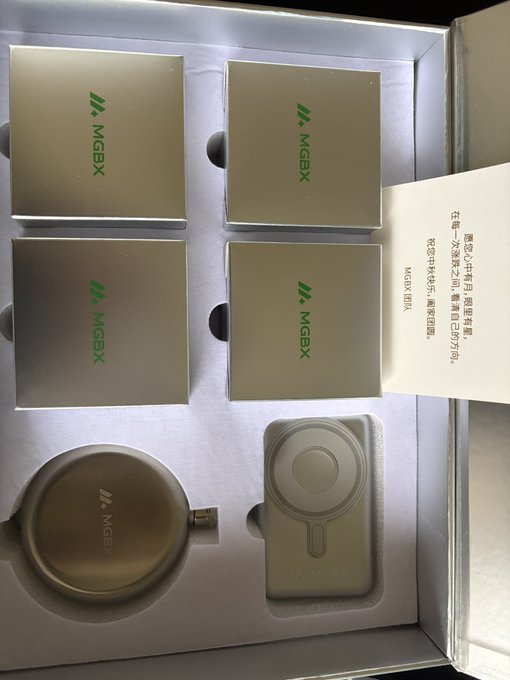 An unboxing of MGBX merchandise shows four silver boxes with green MGBX logos, a silver thermos, and a silver magnetic ring stand, with a card addressed in Chinese to '亲爱的小雅用户 感谢您...'.