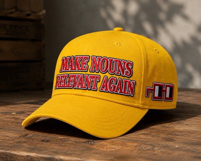 A yellow baseball cap on a wooden surface features the red embroidered text 'MAKE NOUNS RELEVANT AGAIN' alongside a small red-and-black square logo.