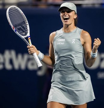 Tennis player Iga Świątek celebrates in a light blue On-running outfit while holding her racket on the court.