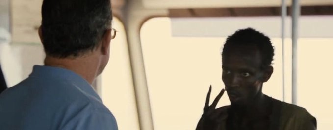 Two men stand facing each other in what appears to be a ship's interior, with one man gesturing with two fingers pointed at his head. The post's caption "Our memecoins own you now" appears to reference the meme "This is Patrick," where Patrick Star taps his temple to signify a clever idea—suggesting that memecoins have cleverly outmaneuvered or "gotten into the heads" of investors, fitting the image's gesture of tapping one's head in a knowing manner.