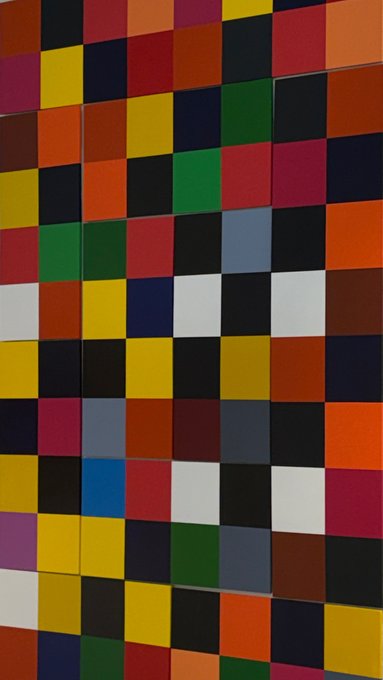 A geometric artwork composed of a grid of colored squares in various hues including red, yellow, blue, green, black, orange, and white, arranged in a colorful mosaic pattern.
