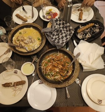 Overhead view of a dinner table set with multiple Middle Eastern dishes including grilled meats, rice dishes, dips, and salads, with multiple place settings.