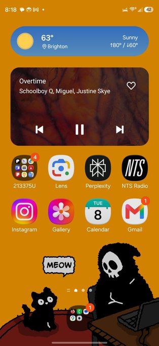 An Android home screen on an orange background showing various app icons, a widget displaying 'Overtime - Schoolboy Q, Miguel, Justine Skye', and a cartoon wallpaper of a cat saying 'MEOW' next to a grim reaper.