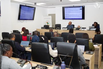 The image shows a group of people sitting at desks, with some using laptops while others are looking at a large screen or a projector. The room appears to be an office setting where they might be working on projects or attending meetings. There are multiple chairs in the room and several TVs mounted on the walls. A few individuals can also be seen wearing ties, suggesting that this gathering may involve professionals dressed for work. The post reads "Auf welche Technischen Herausforderungen seit ihr gestoßen? Mit welchem Digitalen System lässt sich das Vorhaben am besten umsetzen? Wie lange wird es dauern die gesamte Infrastruktur Digital umzustellen?". The post is related to the image as it provides context and background information about the gathering, possibly discussing a project or event in an office setting.