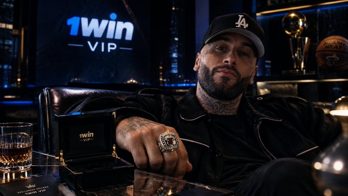 A tattooed man wearing a black LA Dodgers cap and a black jacket displays a large championship ring, seated at a table with a '1win VIP' branded box, glass, and a city skyline backdrop.