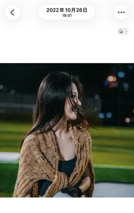 A young woman with long dark hair, wearing a tan knit shawl over a dark top, sits on what appears to be stadium seating at night, her hair blowing in the wind. The image is timestamped "2022年10月26日 18:01" and shows her in a contemplative pose on a sports field, illustrating the post's contrast between her active past on the soccer field in 2022 and her current homebody lifestyle.