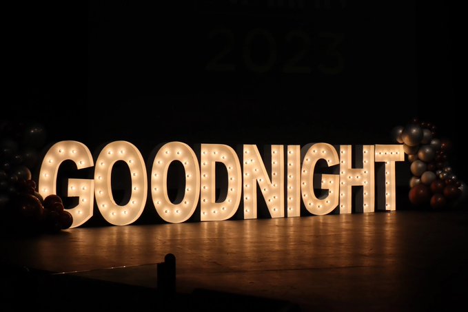 Large illuminated marquee letters spelling "GOODNIGHT" on a stage, decorated with balloons and dim lighting.
