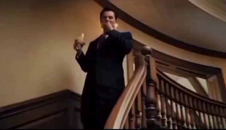 The image shows a man dressed in a suit standing on a staircase, holding a glass of wine or champagne with a mustache. The background features a wooden staircase that leads up to an upper level. The caption "How it feels when you start making people's salary in a day." suggests the post is related to the movie "The Wolf of Wall Street" and possibly discussing the financial aspects of the film, such as the characters' salaries or the importance of money in the story.