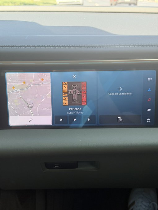 A car's infotainment screen showing a map on the left and a music player displaying the song "Patience" by Guns N' Roses on the right, with "Conecte un teléfono" (Connect a phone) message visible.
