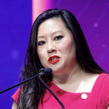 A woman with long black hair, wearing a red top and bold red lipstick, speaks into a microphone against a purple background. The image appears to capture Caroline Pham, MoonPay CLO and former CFTC commissioner, during her remarks at Korea Blockchain Week 2026 about the rapid adoption of tokenized securities.