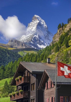 A scenic view of the Matterhorn mountain in Switzerland with a Swiss flag and traditional wooden chalets in the foreground.