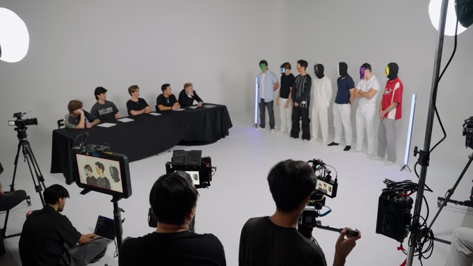 A behind-the-scenes look at a content production set shows a panel of judges seated at a long table facing a lineup of contestants wearing colorful masks, with multiple cameras, lighting equipment, and monitors capturing the scene—though the image's connection to the post's claims about a major wave in trading and onchain activity remains unclear, as no visible text, numbers, or tickers relate directly to the caption.