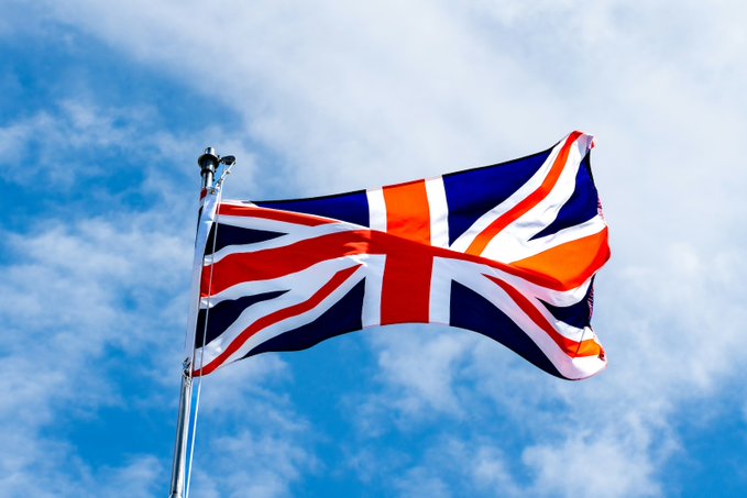 The Union Jack flag flies against a partly cloudy sky, symbolizing the UK's new "no gain, no loss" tax treatment for crypto lending and liquidity pool transactions effective April 6, 2027.