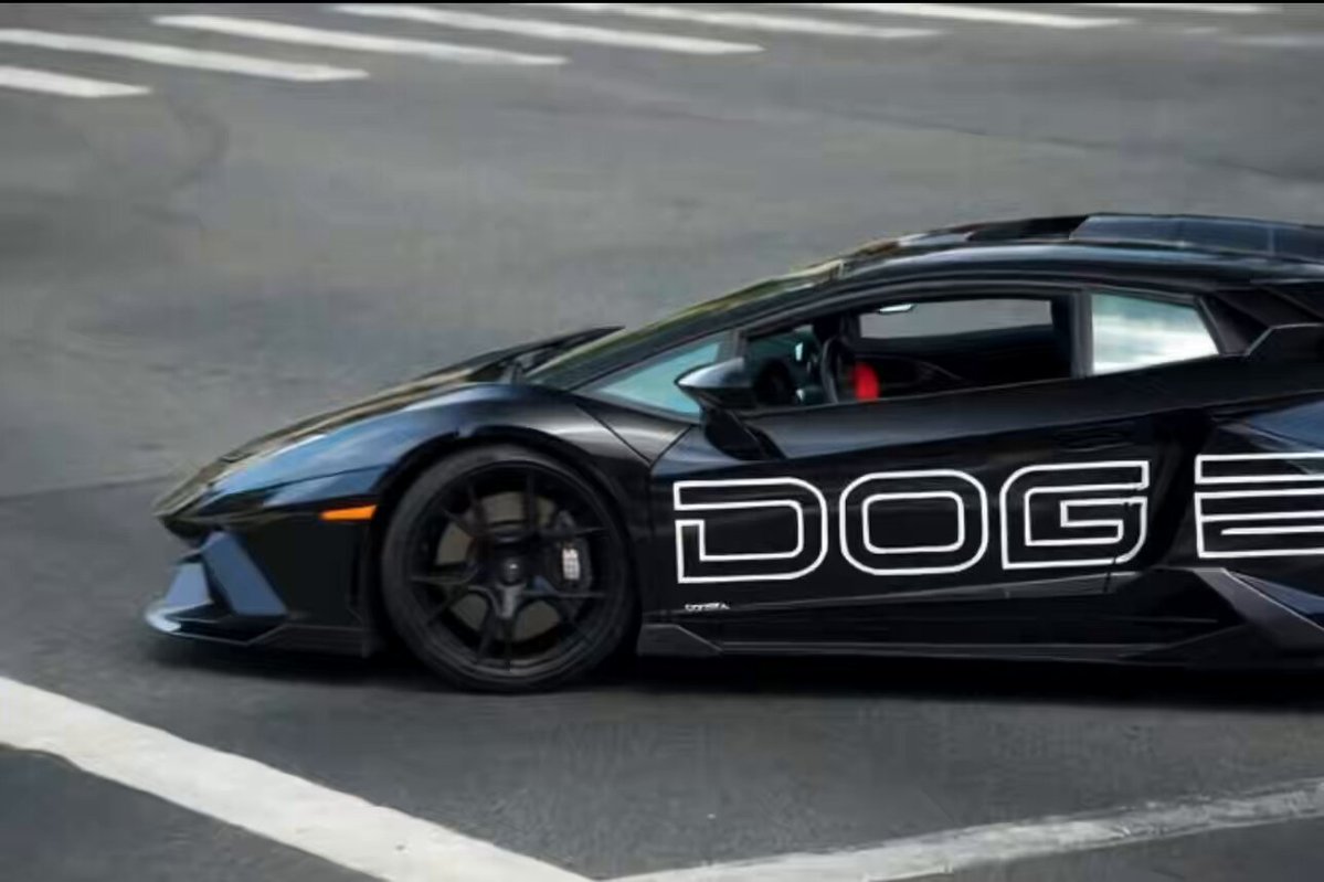 The image features a black Lamborghini sports car driving down a street, with the word "DOGE" prominently displayed on its side. This suggests that the car might be associated with a specific brand or company, possibly related to technology or gaming. The presence of the word "DOGE" in the photo indicates that it is likely an advertisement for this particular vehicle or brand.