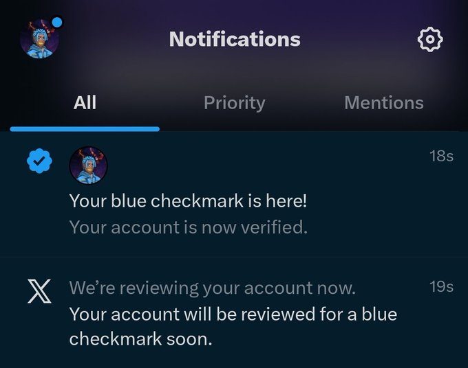 A Twitter/X notifications screen showing a user has received a blue checkmark verification, with messages reading 'Your blue checkmark is here! Your account is now verified.' and 'We're reviewing your account now. Your account will be reviewed for a blue checkmark soon.'