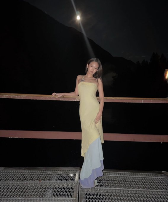 A young woman poses on a bridge at night wearing a flowing yellow and blue gradient dress, with the moon shining brightly in the sky above her. The caption "Polyperps to the mooooon" cleverly plays on the visible moon in the image, using it as a metaphor for skyrocketing perpetual futures in crypto trading.