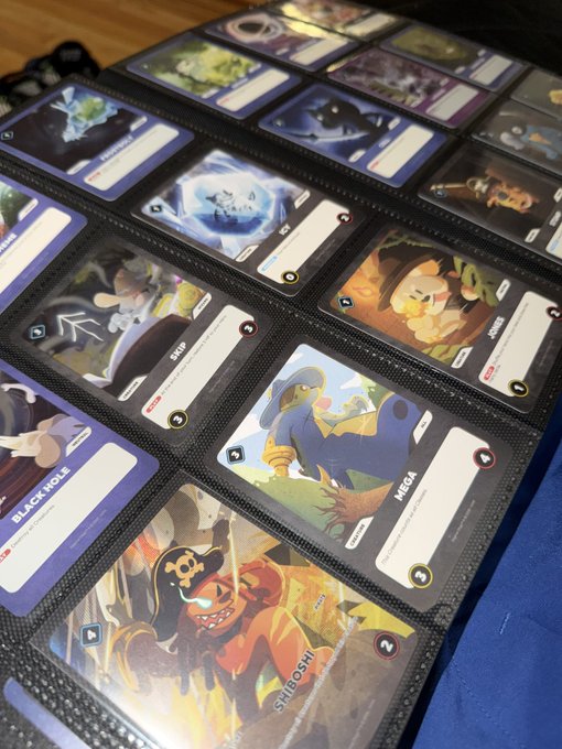 A photograph of a Pokémon trading card binder page showing various cards in protective sleeves, including visible cards labeled 'BLACKHOLE,' 'MEGA,' and 'SHIFTRY,' arranged in a grid layout.