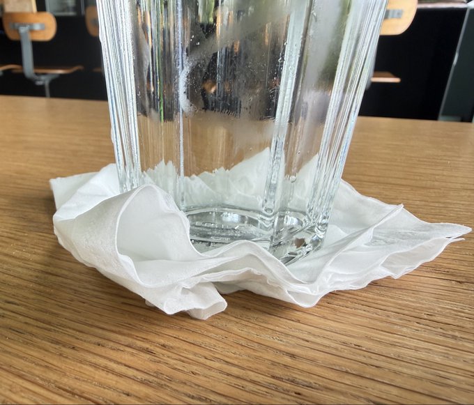 A close-up of an empty, ribbed glass sitting on a crumpled white paper towel on a wooden table.