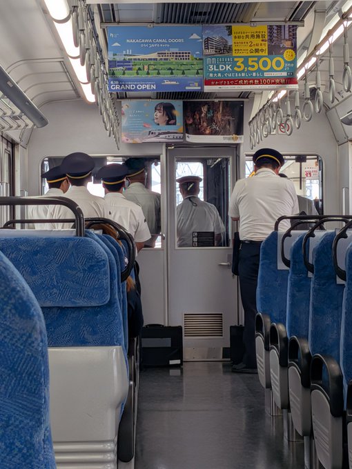 The image shows the interior of a Japanese train carriage, likely in Hakata, with several conductors in uniform gathered near the door while a poster advertises "HAKATAWA CANAL DOORS" residential units at "3,500万円" (35 million yen) for a grand opening. The post's caption suggests asking the conductors for a photo, which fits the scene of multiple uniformed staff gathered together inside the train.
