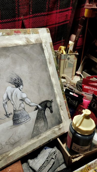 A black and white charcoal or pencil sketch of a muscular figure holding a horse's head sits on a workspace alongside art supplies, including paint tubes (Amsterdam) and a numbered jar marked '24'.